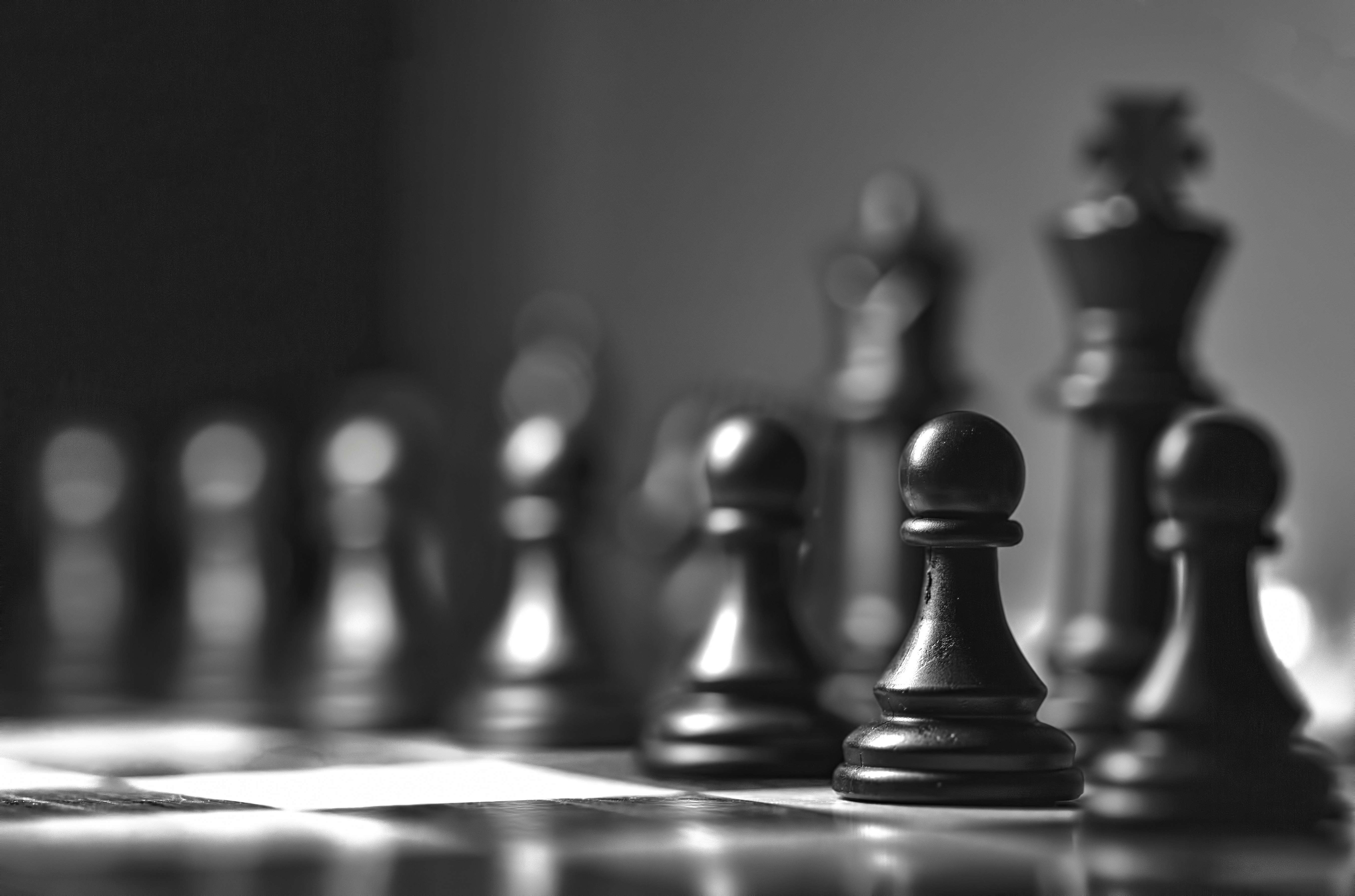 A black pawn in the foreground with other chess pieces blurred in the background.